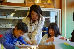 ペーパークラフト教室で、女子学生と一緒に楽しそうに製作に励む児童